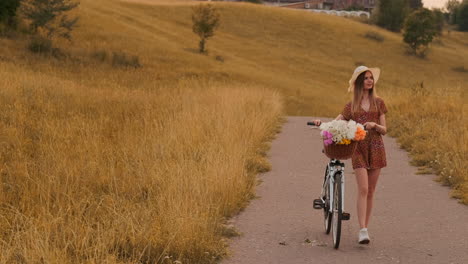 Zeitlupe,-Sexy,-Schöne-Frau-Mit-Einem-Fahrrad,-Einem-Hut-Und-Einem-Leichten-Sommerkleid-Kommt-Mit-Blumen-In-Einem-Korb-Und-Lächelt.
